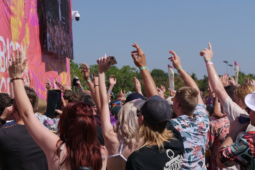 A crowd near the stage stand with arms raised at the festival.