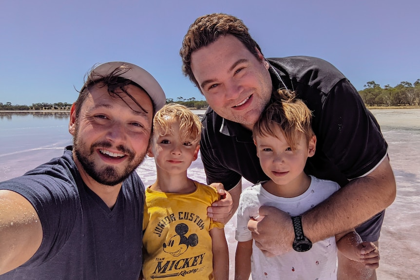 A family photo of two men smiling with their two young boys