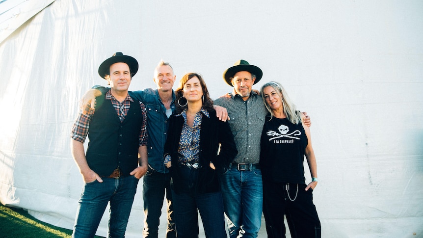 Five members of The Waifs arm in arm outside in front of a big white marquee