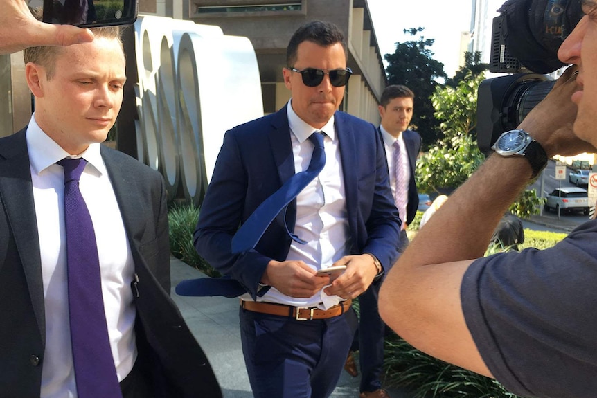 Two men flanked by media as they leave court in Brisbane