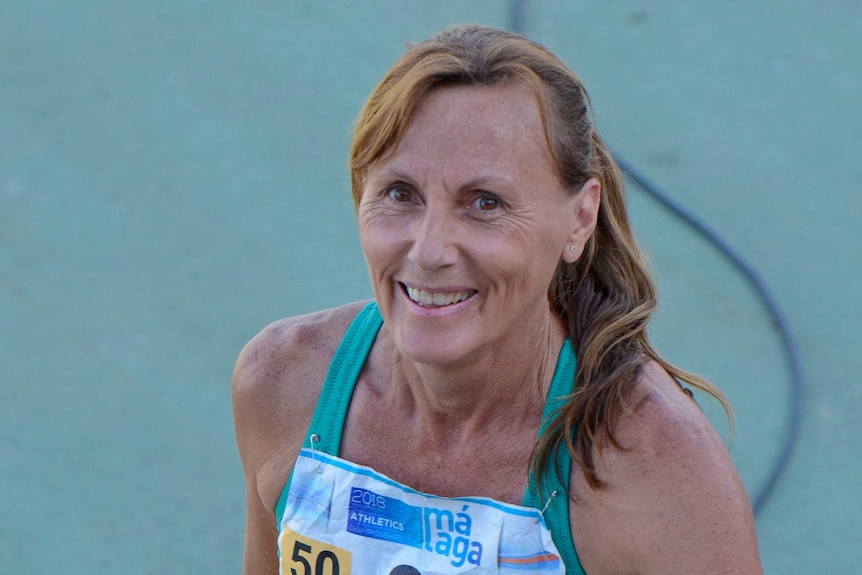 A woman in athletic clothing smiles on track.