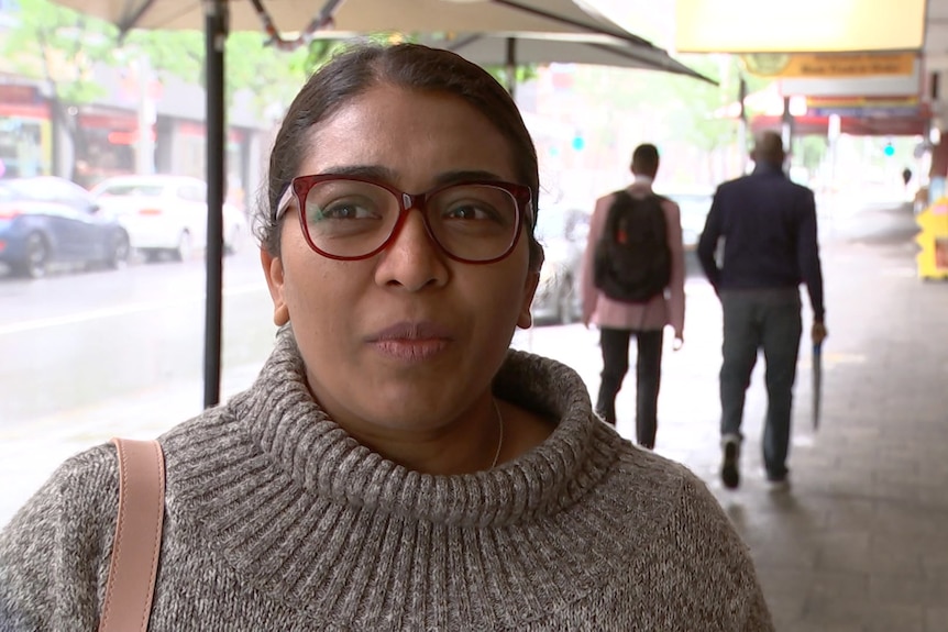 A head and shoulders shot of a woman standing on a high street wearing spectacles and being interviewed.