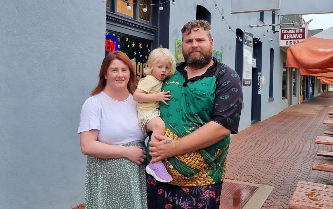A woman, red-haired, stands with her partner, solid build and bearded, and their daughter out the front of their pub.