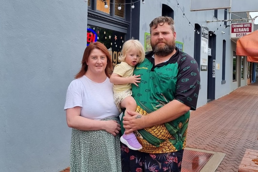 A woman, red-haired, stands with her partner, solid build and bearded, and their daughter out the front of their pub.