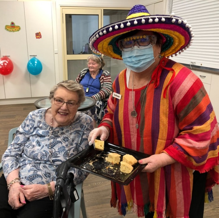 A lady dressed in a poncho and sombrero serves cake to another lady