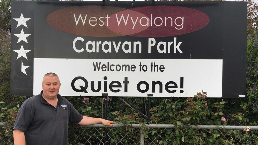 Jamie Adams stands in front of caravan park sign saying "The Quiet One"