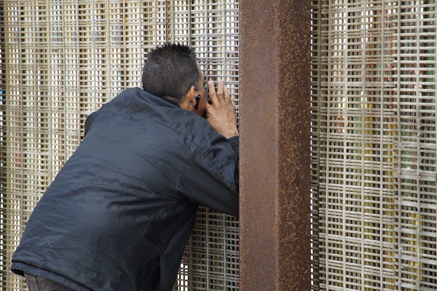 A man tries to kiss his partner through the mesh of the US-Mexico border fence.