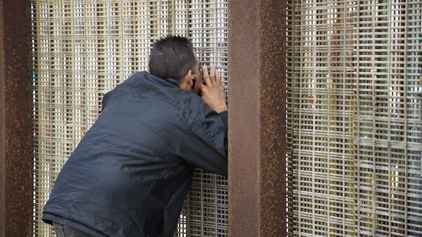 A man tries to kiss his partner through the mesh of the US-Mexico border fence.