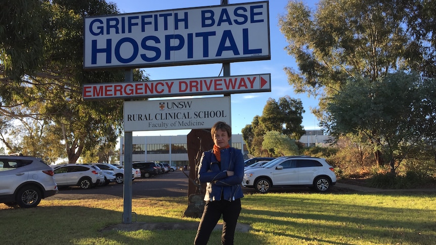 A woman stands with her arms crossed in front of a hospital sign. 