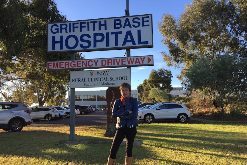 A woman stands with her arms crossed in front of a hospital sign. 