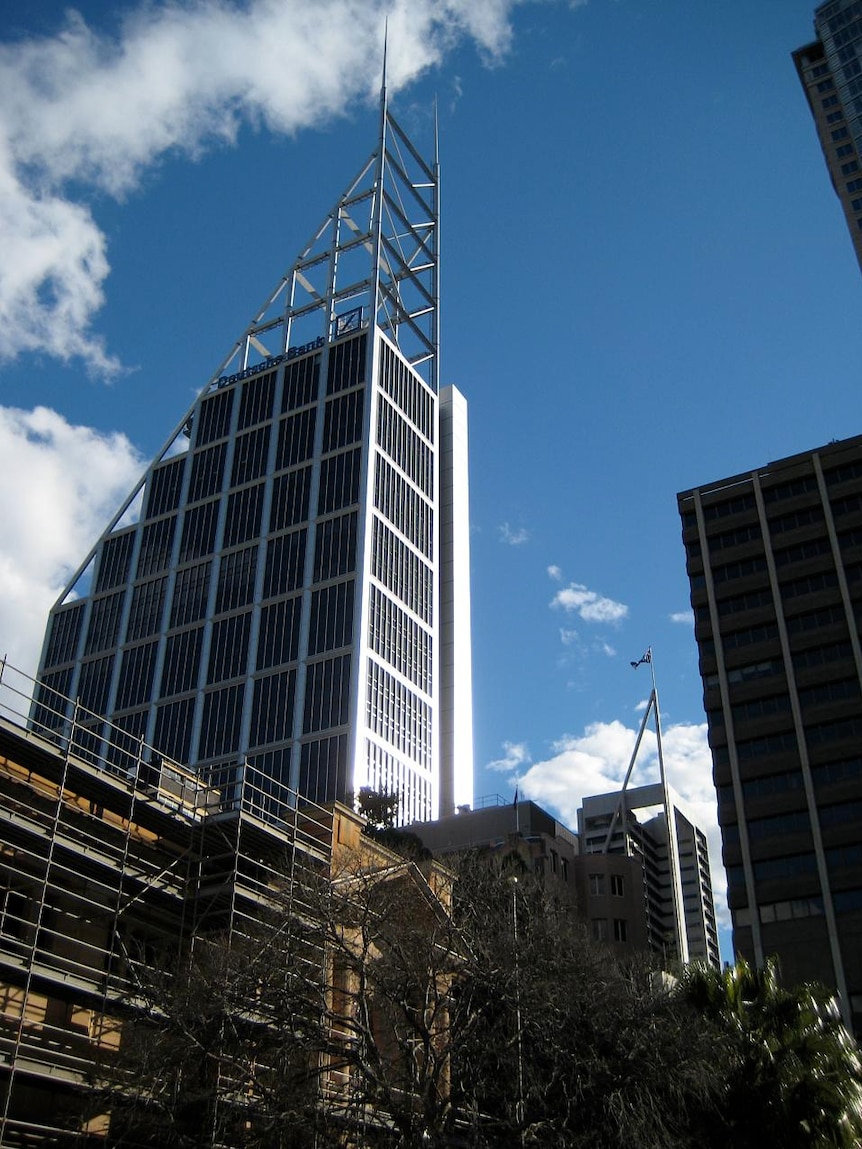 A glass and steel skyscraper with a triangular top is pictured against a bright blue sky.