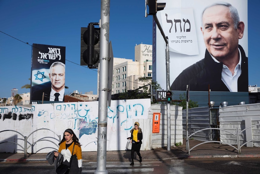People walk next to election campaign billboards showing Israeli Prime Minister Benjamin Netanyahu and his opponent Benny Gantz.