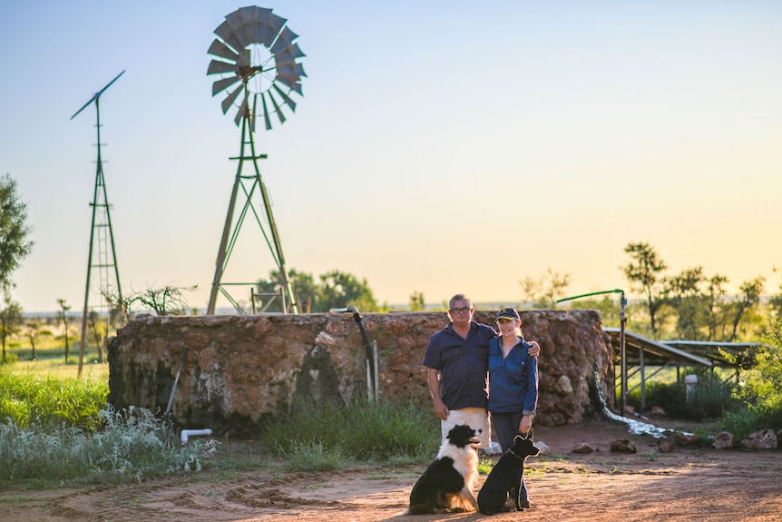 Two people stand with their two dogs at Giralia station, in front of a windmill.