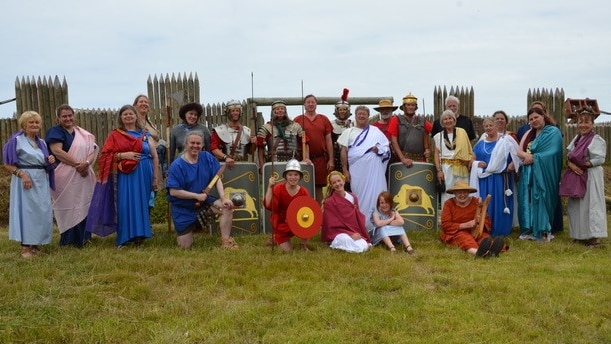 People Dressed in Roman costume pose for a photo in front of a walled arena 
