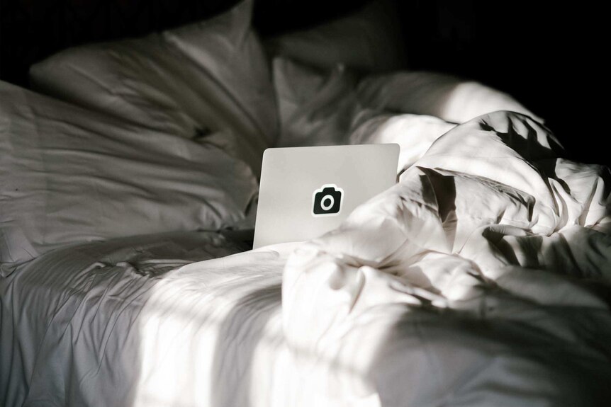 A laptop on a bed with rumpled sheets to depict the role blue light can play in sleep problems.