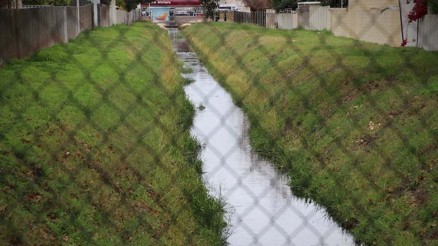 A stormwater drain sits behind a fence