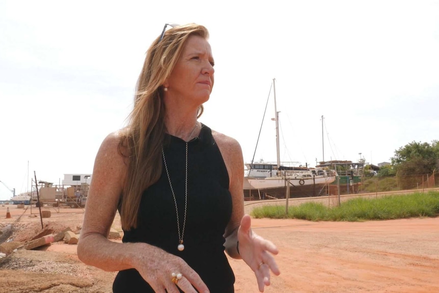 A woman stands in front of a boat yard