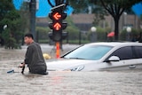A man rides a bicycle through a flooded intersection.