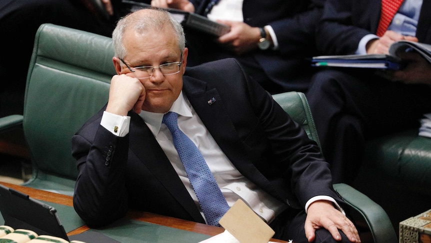Scott Morrison leans his head on his hand and looks across towards the opposition in Question Time
