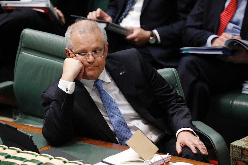 Scott Morrison leans his head on his hand and looks across towards the opposition in Question Time