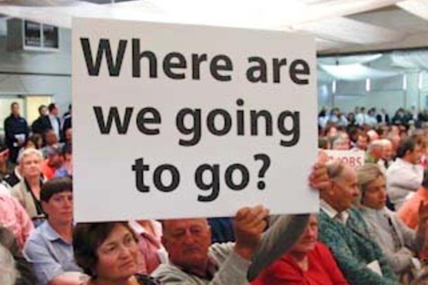 People at a public meeting holding a sign.