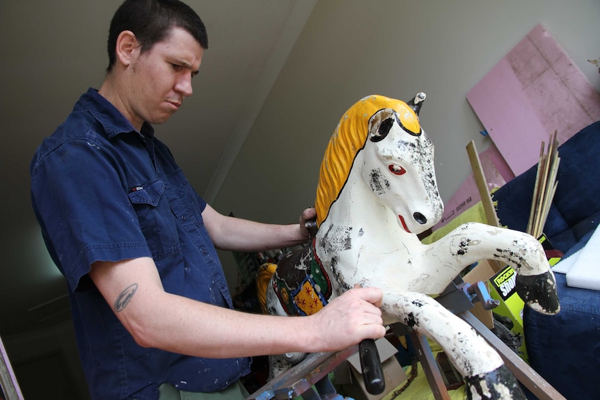 Repairer Jason Coultis holds and repairs a carousel horse.