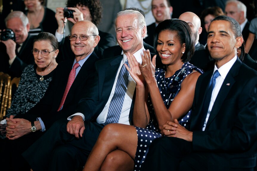 A group of people dressed in smart clothes sit in the front row of a hall