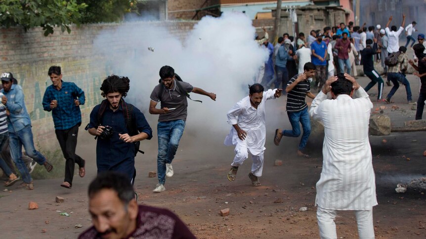 people run away from an tear gas shell that has exploded in the streets of Kashmir.