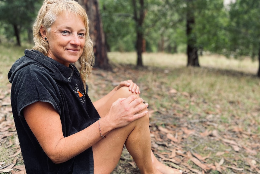 Woman sitting on the ground with hands on knees and looking at the camera.