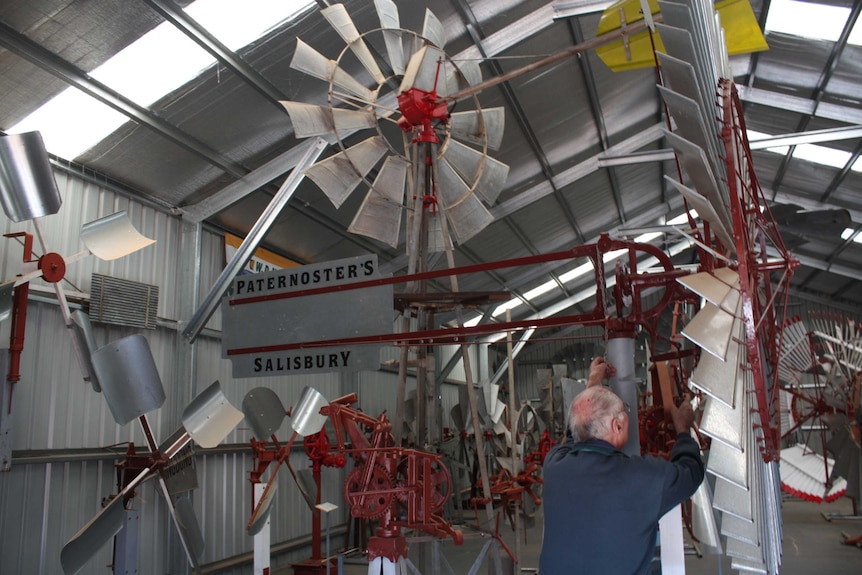 A man tinkers in a large outback shed full of windmills.