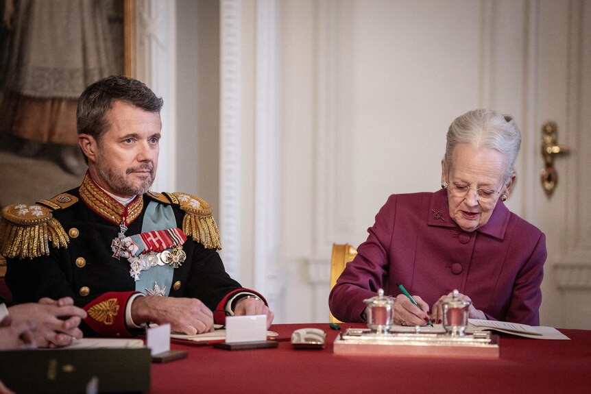 A man sits next to a woman signing forms 