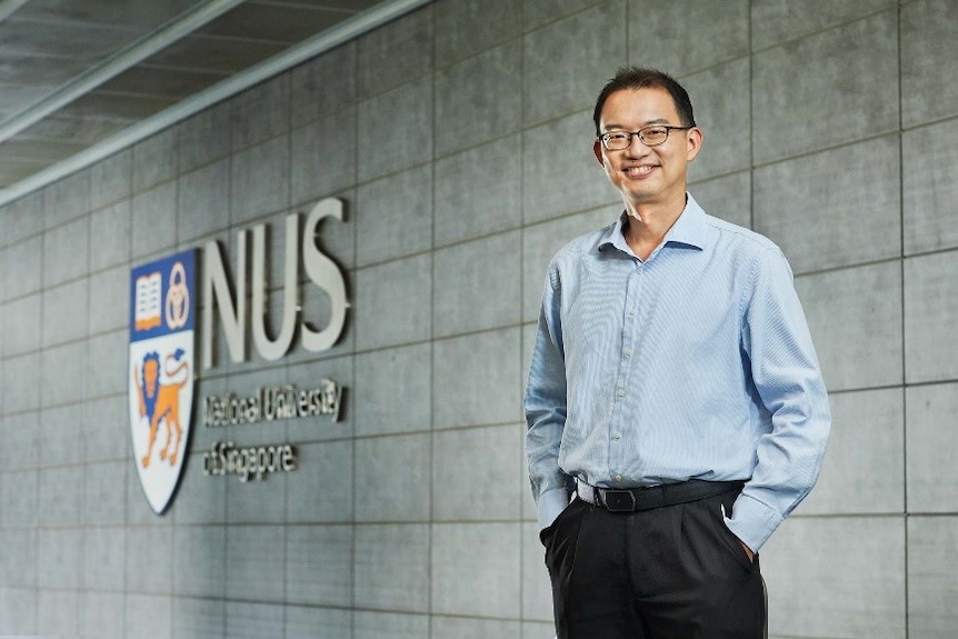 A man poses for a photo next to a National University of Singapore banner