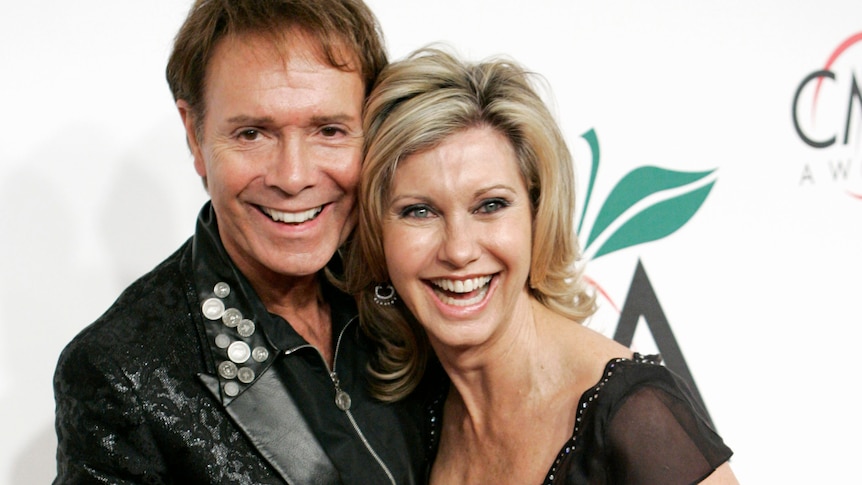 Olivia Newton-John smiles as she holds Cliff Richard's hand at a red carpet event