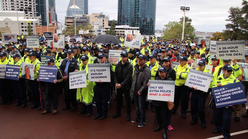 Hundreds of police officers wearing caps and holding placards at a rally.