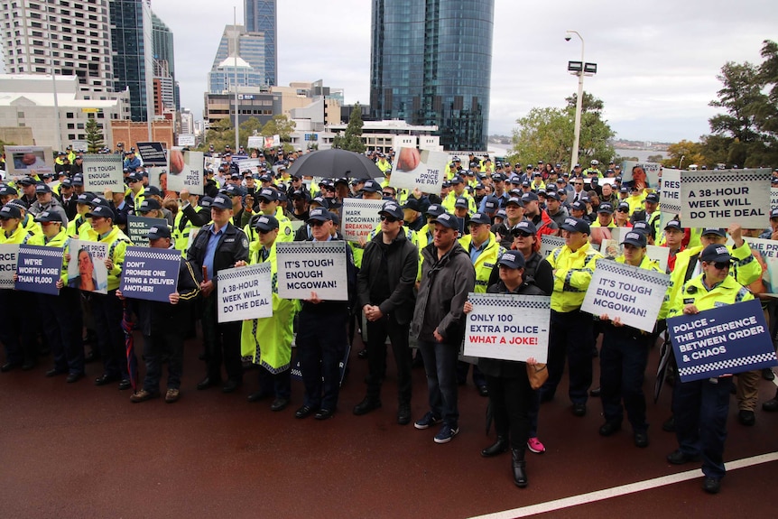 Hundreds of police officers wearing caps and holding placards at a rally.