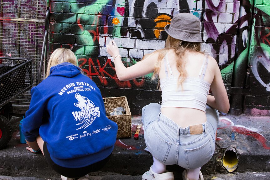 Mia and Eliza squatting in Hosier Lane, adding to artwork with paintbrushes