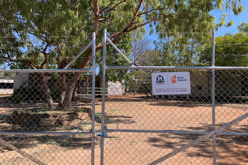 a locked gate with a TAFE sign with buildings in the background