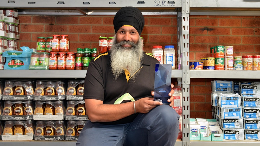 Man kneels in front of stacks of jars and cans. 