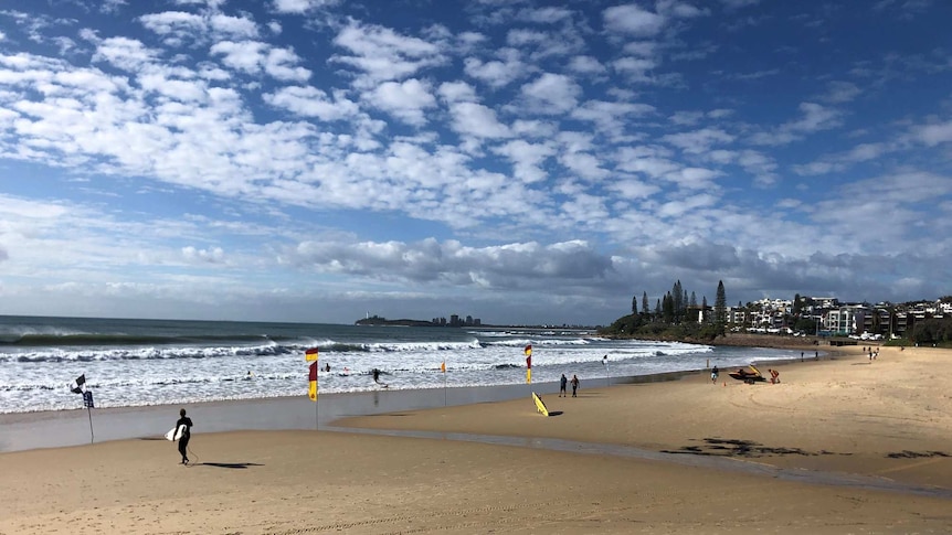 People walk along the beach at Alexandra Headland.