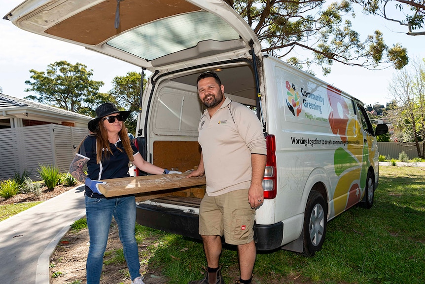 A woman and a man removing timber from the back of a van.