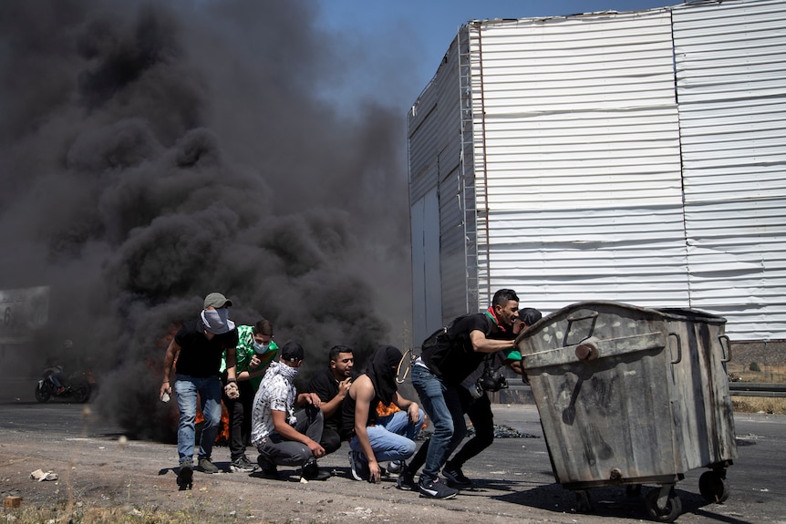 Protesters behind an industrial bin a tyres burn behind them.