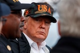 An elderly man wears a cap with green, brown and tan camouflage patterns and large orange letters spelling out USA