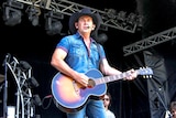 A man in double denim and a cowboy hat plays guitar onstage.