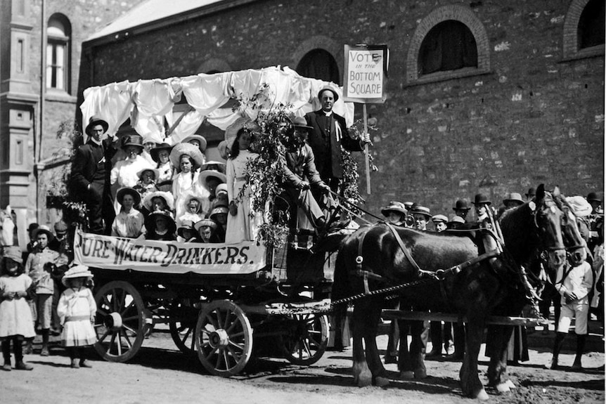 A black and white image of a float in a parade displaying a banner reading 'pure water drinkers'.