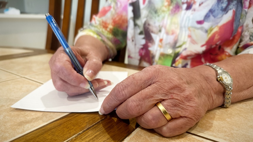A woman hands writes a letter at a table