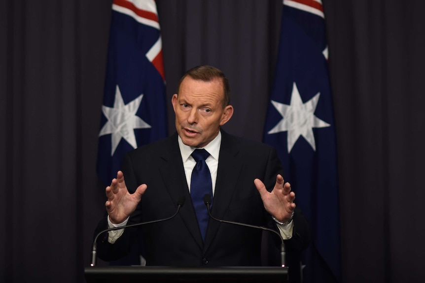 Man stands before two Australian flags, speaking