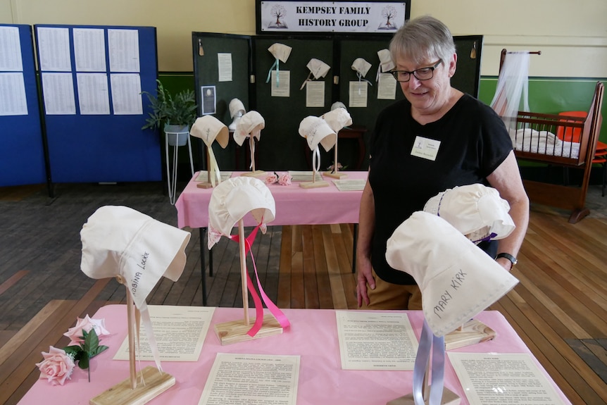 A woman stands among a display of old-fashioned bonnets, made in honour of convict women.