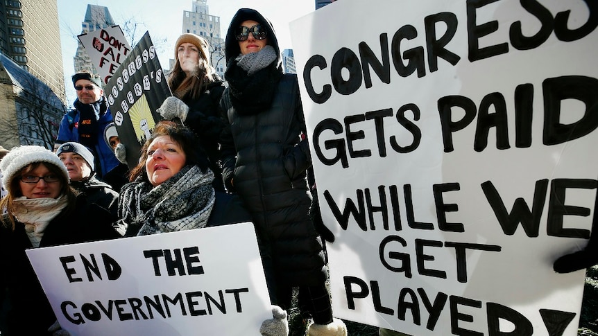 People holding protest placards stand closely together in the middle of a built up city.