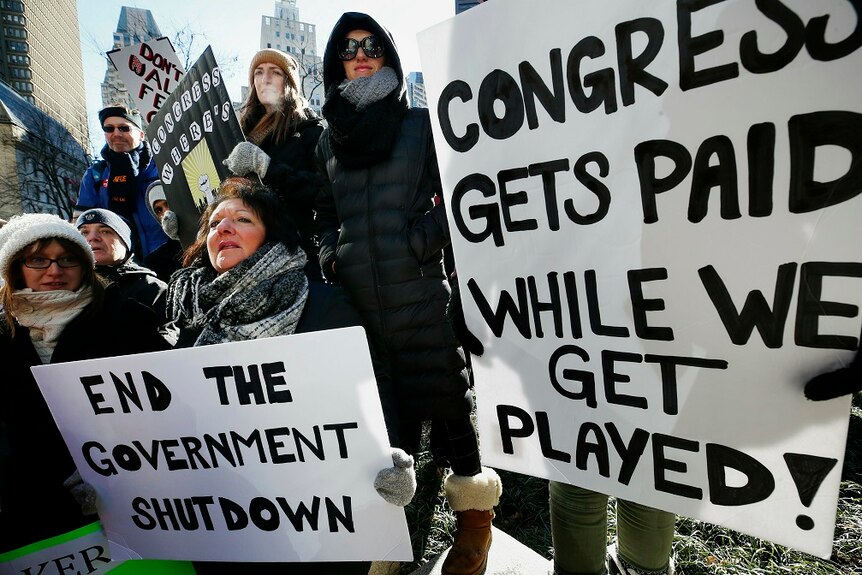 People holding protest placards stand closely together in the middle of a built up city.