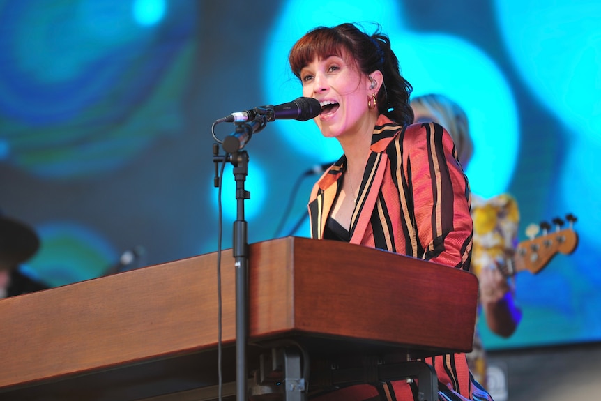 A woman singing into a microphone behind a keyboard on a stage
